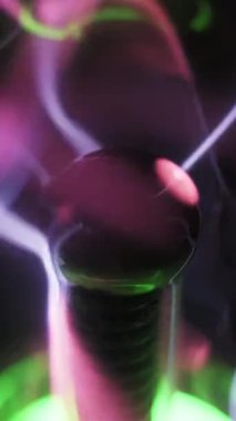 Plazma küresindeki merkezi elektrotun makro görüntüsü. Pembe ve mor ışık telleri dışarı doğru yayılıyor. Elektrik akımları iyonize gazın içinden geçerken. Karanlık bir uzayda yüksek voltajlı enerji boşalması.