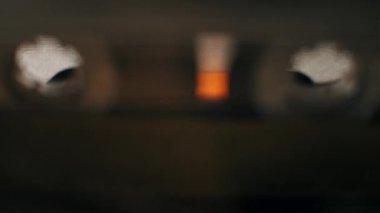 Bir elin klasik bir teybi açarken, eski sarı bir kaset yerleştirirken ve kapıyı kapatırken görüntüsü. Oyuncu mekanizması, bobinlerin dönen güneş ışığıyla hareket eden gölgeler oluşturmasıyla devreye girer..