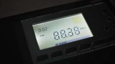 Dijital radyo ayarlayıcılarının makro yakın plan LCD ekran görüntüsü karanlık bir odada FM frekanslarını hızla tarıyor. Numaralar alıcıdaki bir yayın sinyalini ararken hızla değişir..