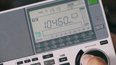 Modern taşınabilir radyo alıcısını ayarlayan birinin yakın çekimi. LCD ekran, FM frekans numaralarının hızla değişerek görünür bir sinyal ölçer ile bir yayın istasyonu aramasını gösterir.