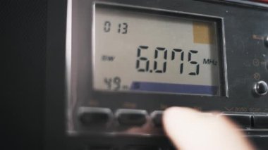 Dijital alıcıda radyo bantları arasında geçiş yapmak için tuşlara basan makro bir parmak. LCD ekran döngüleri, ayarlamadan önce MHz ve kHz birimlerini gösteren FM MW LW ve SW kiplerinde dolaşır.