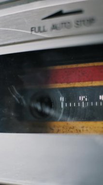 Dikey, yakın plan sarı ses kaseti. Gümüş bir çalgıcıda ileri sarar. Hızla dönen makara retro elektronik cihazın içinde hareket bulanıklığına dönüşür..