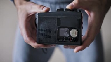 Siyah antika bir kasetçaları tutan bir adamın yakın çekimi. Küçük kaset makaraları taşınabilir ses kayıt cihazının içinde görünür bir şekilde dönüyor..