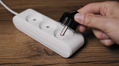 Yüksek açılı beyaz plastik uzatma kablosu koyu kereste zemininde ya da masada duruyor. Standart bir siyah kablo bir ev veya ofis kurulumunda çoklu aygıtlar için bir elektrik devresi oluşturur
