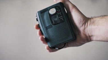 Sade bir arka planda dönen bant makaralı eski bir mikrokaset kaydediciyi tutan bir elin yakın çekimi. Bu retro ses cihazı gazeteciliği, casusluğu ve analog teknolojiyi temsil ediyor..