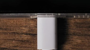 Beyaz bir USBC kablosunu akıllı telefondan açık bir çantada çıkartırken makro çekilen bir el görüntüsü. Cihaz portu, kahverengi ahşap masadaki güç kaynağından ekran kapalıyken ayrılır.