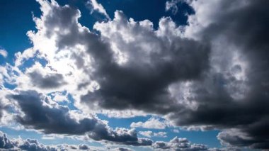 Düşük açılı koyu gri ve beyaz kümülüs bulutları parlak güneşi periyodik olarak engelliyor, atmosferde dramatik ışık kaymaları ve güneş ışınları yaratıyor..