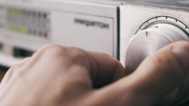 Bir elin, fırçalanmış metal ses düğmesini eski bir stereo yükselticinin ses seviyesini aşağı yukarı çevirerek ayarlaması. Arka plan gümüş birimde odak dışı bir LED ölçer gösteriyor.