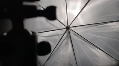 Yakından çekilen bebek beyaz yarı saydam bir fotoğraf şemsiyesine bastırıyor. Siyah metal kaburgalar ve merkez göbek ön planda siluetli bir ışık standı ve kumaştan yayılan parlak bir ışık ile görülebilir..