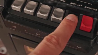 Retro teypteki gümüş durdurma düğmesine basarak sarı etiketli bir kaset çıkarıyoruz. Almanca metin kontrollerini, desenli bir siyah panel ve kapı eylemini gösterir.