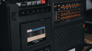 El kapatma düğmesine bas, siyah bir retro teypten ses kaseti çıkar, bandı klasik mavi ve beyaz etiketiyle çıkar, ve sonra boş güverte kapısını kapat.