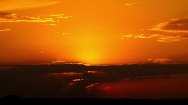 Yoğun, karanlık bulutların ardında kaybolan turuncu güneşin zamanı. Karanlık, siluetli bir ufkun üzerinde akşam gökyüzünde çarpıcı bir sıcak parıltı bırakıyor..