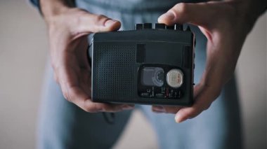Kaset içeride dönerken, elinde siyah portatif bir kasetçalar tutan erkek ellerinin yakınlaşması. Bu antika cihaz eski röportaj ekipmanları, gazetecilik, analog ses ve casus teknolojisinin sembolüdür..