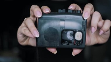 Makaralar içeride dönerken, kadın ellerinin portatif bir ses kaydedici tutarken doğrudan görüntüsü. Bu klasik 90 'ların aleti 2000' lerin nostaljisini, 2000 'lerin modasını ve klasik elektronik aletlerini çağrıştırıyor..