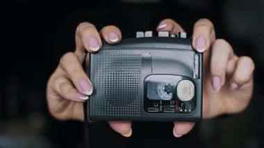 Manikürlü ellerin siyah portatif bir kasetçalar tutarken ön görüntüsü ve içinde bant makaraları dönüyor. Bu retro ses aygıtı 90 'lar ve 2000' lerin müziğini, nostaljisini ve Y2K modasını temsil eder..