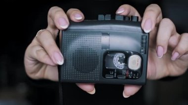 Fransız manikürlü kadın eli, eski taşınabilir bir kaset kaydedici tutuyor. Aygıt koyu bir arkaplana karşı ses çalarken ya da kaydederken bant dönüyor.