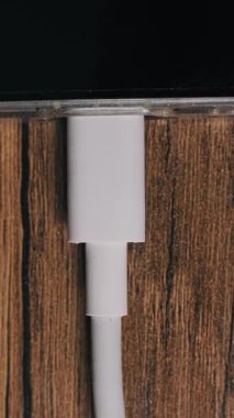 Dikey, yukarıdan aşağıya doğru çekilen parmaklar akıllı telefon portundan beyaz bir USB-C kablosu çekiyor. Ekran, ahşap masadaki güç kaynağından cihazı ayıran hızlı şarj yüzdesi göstergesini gösteriyor.
