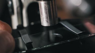 Metal klipslerle korunan mikroskop sahnesine cam kaydırak yerleştiren makro parmaklar. Bir pipet kimyasal analiz için temiz bir sıvı ya da Bokeh renklerine sahip bir laboratuvarda bilimsel bir prosedür ekler..