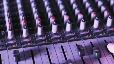 Bir prodüktörün faders kanalını profesyonel bir ses karıştırıcı konsolu üzerinde ayarlarken, karanlık bir yayın ortamında dinamik pembe ve turuncu ışık altındaki düğmeler ve düğmeler kullanılıyor..