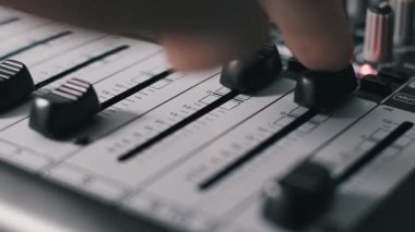 Profesyonel bir ses karıştırma tahtasında iki fader aşağı çeken parmaklar makro açılı görünümü desibel ölçeği ve numaralandırılmış kanallar gösteriyor. Hareket, bir stüdyo seansında sesi kısmayı gösteriyor.