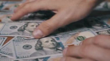 Erkek ellerine yakından bak. Tahta masadaki 100 dolarlık banknotları hızlıca say. Bu durum zenginlik, gelir, kar, tasarruf ve başarılı ticari işlemleri temsil etmektedir.