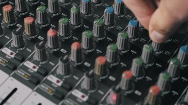 Ses mühendisinin yüksek açılı görüntüsü bir ses karıştırma konsolunda renk kodlu düğmeleri döndürerek kayıt sırasında yüksek ve düşük frekans ayarlarını ayarlıyor.