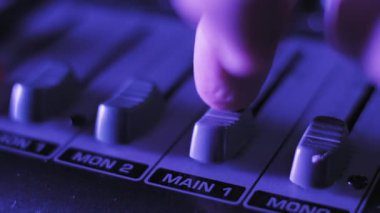 DJ parmağının aşırı yakın plan görüntüsü MAIN 1 fader 'ı profesyonel bir ses panosuna bastırıyor desibel işaretleyicilerle ses ayarlarını ayarlıyor mor ve turuncu konseri değiştiren ışığın altında görünüyor..