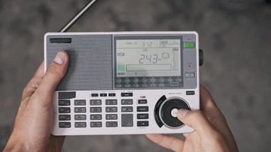 Çok bantlı bir radyo alıcısında kullanıcı değiştirme kiplerinin yukarıdan aşağı görünümü. Eller, LW MW SW ve FM bantları için frekans ve kipteki değişiklikleri yansıtan dijital LCD ekranlı düğmelere basar.