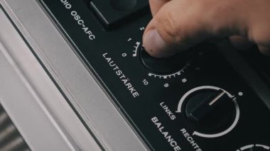 Siyah Lautstarke ses düğmesini eski bir Alman ses sistemine çeviren bir elin yüksek açılı görüntüsü, denge kontrolünün yanındaki numaralandırılmış ölçekte ayarlanıyor..