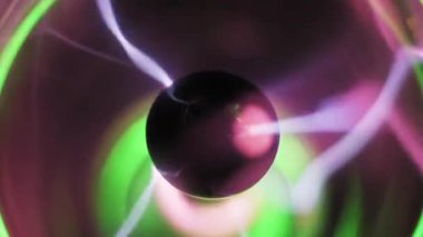 Pembe ve mor elektrik cıvataları yayan plazma topu merkezi elektrotun makro görüntüsü. Dalgalı iyonize gaz telleri ve koyu arkaplanda yeşil ışık parlayan flamalar. Yüksek voltaj enerji gösterimi.