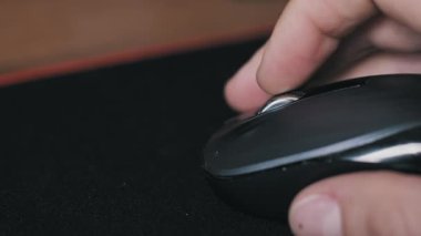 Bir düğmeye basan bir erkek elin makro görüntüsü ve siyah kablosuz bir farenin metal çarkını kumaş bir farenin üzerinde kaydırması. Ofis işi ve oyun teknolojisi ekipmanları ayrıntıları.