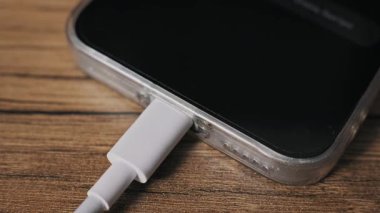 Makro, beyaz bir USB-C güç kablosunu açık bir çantada akıllı telefondan ayırırken elini vurdu. Aygıt ekranında bir pil seviyesi göstergesi simgesi var, hepsi tahta bir masa yüzeyinde.