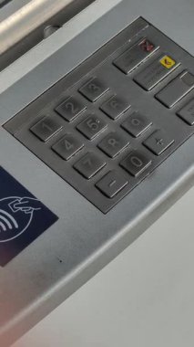 Bir ATM makinesinin metal tuş takımının dikey, açılı yakın çekimi. Güvenli PIN kodu girişi için sayısal düğmeler, NFC 'nin erişilemez ödeme sembolü var. Bankacılık teknolojisi ve işlem güvenliği kavramı.