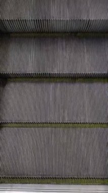 Tepetaklak perspektif yürüyen yürüyen merdiven çelik ahenk dokusu sarı güvenlik çizgileri sürekli toplu taşıma mekanizması ayaklar siyah ayakkabılar modern kentsel altyapı seyahat yolcusu gibi görünüyor.