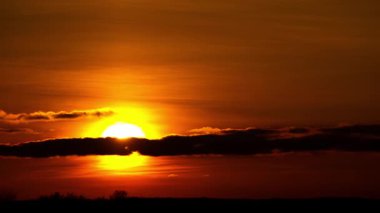 Parlak turuncu güneşin altın saatinde kara bulutların ardında batışının zamanı. Ufuk çizgisinde yoğun atmosferik ışıltı. Zamanın geçişi, iklim değişikliği ve doğal güzellik kavramları.