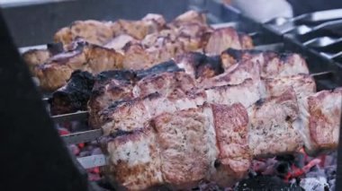 Terbiye edilmiş et şişleri, kızgın kömür közleri üzerinde metal ızgarada pişerken yakından görülüyor. Browning pork veya beef shashlik parçaları etrafında kalın duman yükselir.