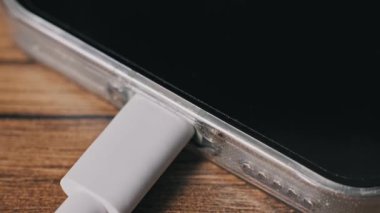 Şeffaf bir çantadaki cep telefonundan beyaz bir USB-C veri kablosunun fişini çeken bir elin makro görüntüsü. Aygıt bağlantıyı kestiğinde ekran bir yük yüzdesi bildirimi gösterir.