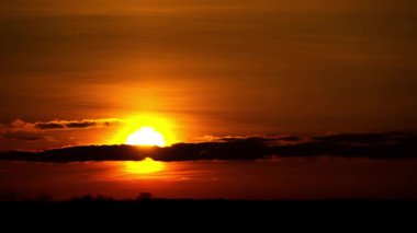 Güneşin kara bulutların ardında batışı, kuşların canlı turuncu gökyüzünde uçuşu. Atmosferik alacakaranlık parıltısıyla siluetli bir manzara. Doğanın kavramları, özgürlük ve günün sonu..