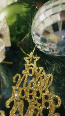 Altın parıltısı Mutlu Noeller süsü bir disko topunun yanındaki süslü ağaca asılı. Sığ alan derinliğine sahip yakın çekim ışıl ışıl detayları ve sıcak tatil ışıklarını gözler önüne seriyor..