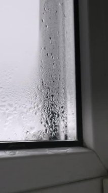 Soğuk bir pencere camından aşağı süzülen su damlacıklarıyla yoğun yoğunlaşma. Bulanık, gri arka plan dışarıda soğuk ve yağmurlu bir gün olduğunu gösteriyor..