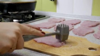 Dişi eller tahta bir tahta üzerinde çiğ domuz pirzolası dövmek ve yumuşatmak için metal bir çekiç kullanır. Yakın çekim, yemek hazırlama sürecini bir ev mutfağında yakalıyor..
