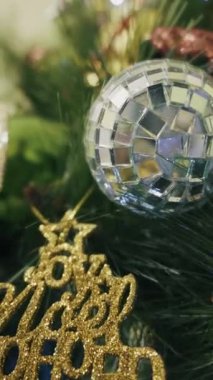 Madalyalı Noel ağacında gümüş bir disko topu ve altın bir simli tabela yer alıyor. Yumuşak odak arka plandaki süsten öne doğru çekilerek neşeli bir bokeh oluşturur.