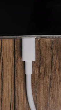 Bir elin dikey makro görüntüsü beyaz bir USB-C kablosunu ahşap bir yüzeydeki bir cihaz kapağından çıkarıyor. Aygıt gücü keserken ekranda şarj durumu yüzdesi görüntülenir.