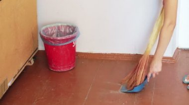 Süpürgesi olan kız yerde enkaz süpürür ve çöp toz içine atar.