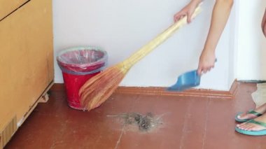 Süpürgesi olan kız yerde enkaz süpürür ve çöp toz içine atar.