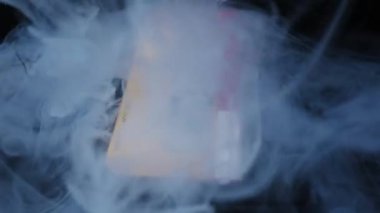 Yıpranmış sarı etiketli klasik ses kaseti beyaz duman tarafından yutulur. Karanlık bir arkaplanda, atmosferik, karamsar ışıklandırmayla yakın çekim..