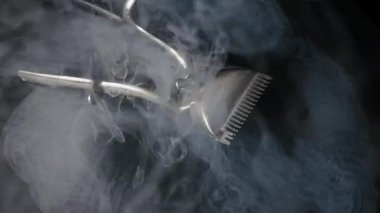 Karanlık bir yüzey üzerindeki klasik el yapımı saç makasıyla kalın beyaz duman kaplanır. Esrarengiz buhar, metalik berber aletinin etrafında dramatik bir yavaş çekim ile dönüyor..