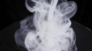 Üzerinde siyah bir ağızlık bulunan beyaz elektronik sigara kalın dumanlar arasında dönüyor. Dramatik stüdyo ışıkları, zifiri karanlık arka planda dönen buharı aydınlatıyor..