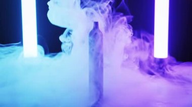 Tek kullanımlık elektronik sigara kalın ve dalgalı dumanla çevrili yansıtıcı bir yüzeyde duruyor. Dikey neon boru ışıkları sahneyi aydınlatıyor, canlı bir şekilde, buhar üzerine renk değiştiriyor..