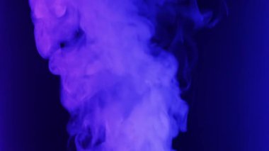 Yoğun duman bulutu siyah bir zemine doğru yükselir ve kıvrılır. Duman, değişen neon ışıklarıyla aydınlanıyor, mavi ve mordan yeşile dönüşüyor..